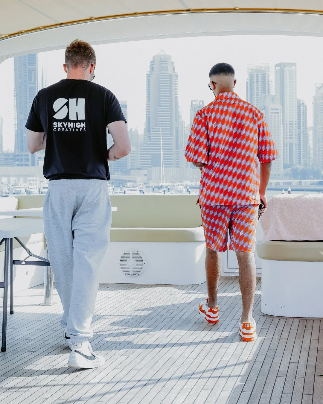 Two members of the SkyHigh Creatives team on a yacht deck, facing a city skyline